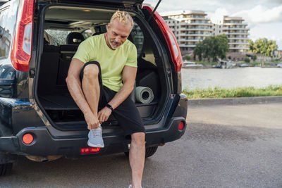 Man tying shoelace sitting in trunk of car