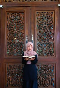 Portrait of woman reading koran while standing against closed door