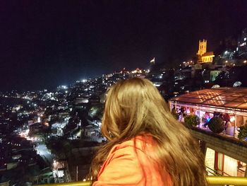 Rear view of woman against illuminated buildings at night