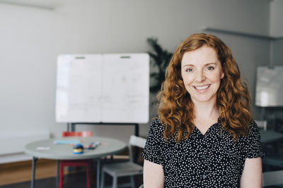 Portrait of confident redhead businesswoman standing at creative office