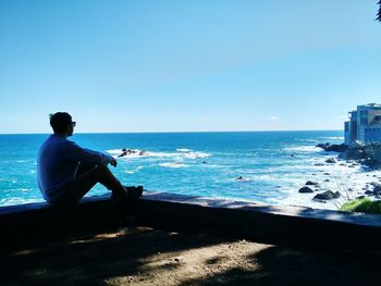 Man sitting on beach against clear blue sky