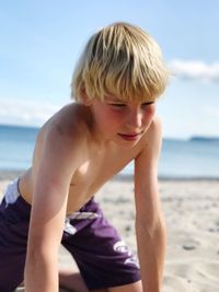 Shirtless teenage boy kneeling at beach