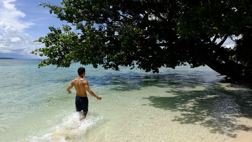 Rear view of shirtless man walking in sea against sky