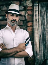 Portrait of man wearing hat standing against wall