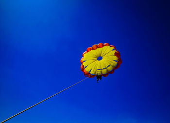 Low angle view of people parasailing against blue sky