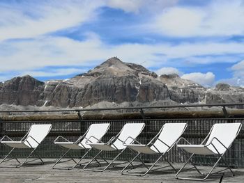Empty deck  chairs on dolomite mountain against sky