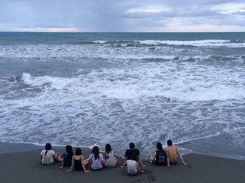 Rear view of friends sitting at beach against sky