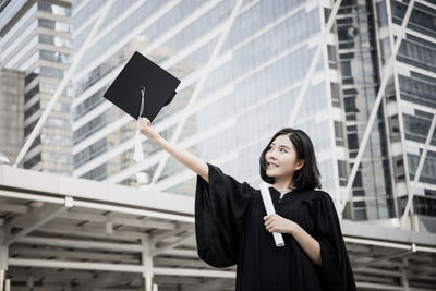 Young woman wearing black graduation gown standing in city