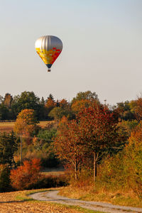 Hot air balloon flying over trees against clear sky
