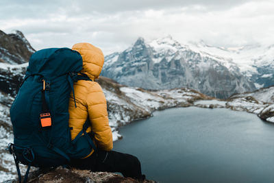 Rear view of man standing on snowcapped mountain against sky