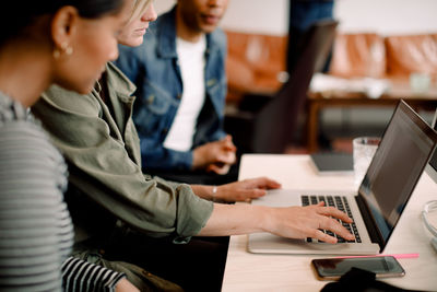 Female executive using laptop while sitting by coworkers at desk in office