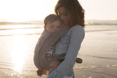 Mother carrying son in baby carrier while standing at beach