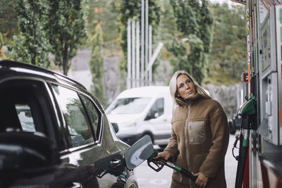 Mature woman pumping gas in car while standing at fuel station