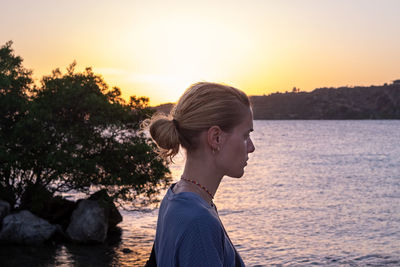 Side view of woman looking at lake during sunset