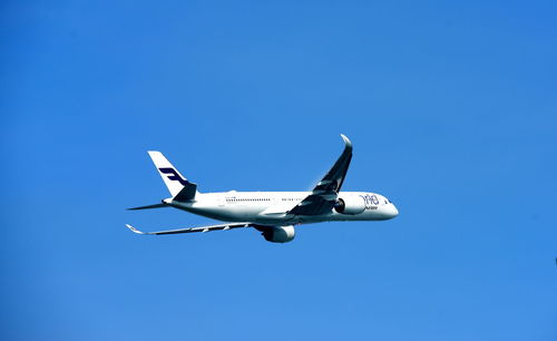 Low angle view of airplane flying against clear blue sky