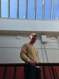 Low angle view of man standing by railing against skylight