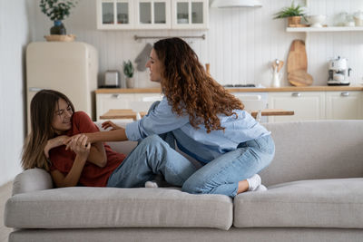 Friendly caucasian woman and teenage girl entertain themselves sits on sofa in spacious bright house