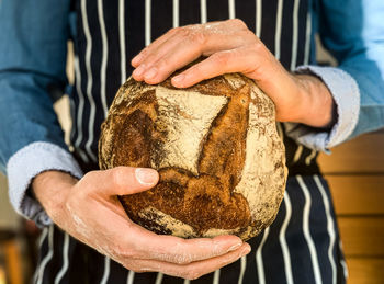 A man in stripped blue apron is holding freshly baked sourdough bread. traditional french loaf