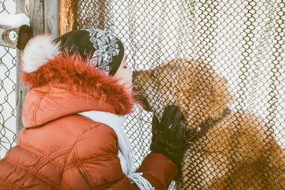 Young woman kissing dog through wire mesh