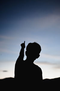 Vertical silhouette in golden hour of young man point his finger to the sky