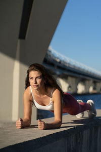 Full length of woman exercising by river against bridge