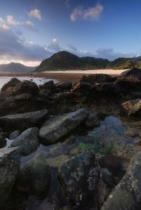 Rocks on beach against sky during sunset