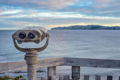 Coin-operated binoculars by sea against sky