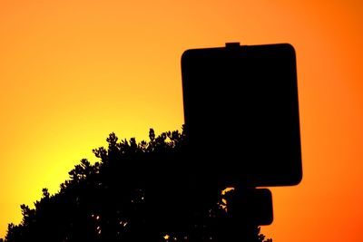 Low angle view of silhouette telephone pole against orange sky