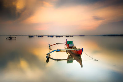 Boat moored in lake against sky during sunset