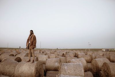 Portrait of man standing on hay bales on field against sky