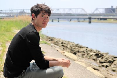 Portrait of young man sitting outdoors by river