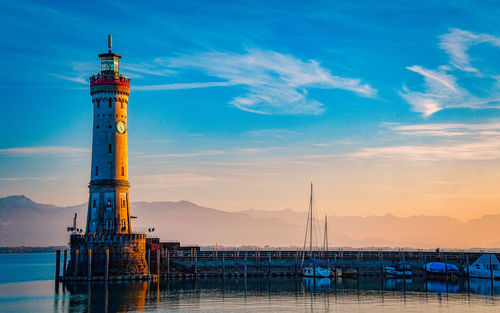Lighthouse by sea against sky during sunset