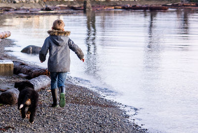 Rear view of boy with dog running at lakeshore during sunset