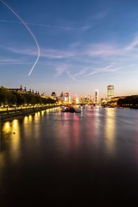 Illuminated city by river against sky at night
