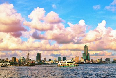 View of city at waterfront against cloudy sky