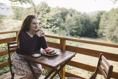 Young woman drinking coffee on wooden house balcony