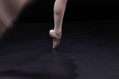 Low section of ballet dancer dancing against black background