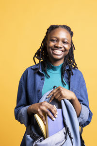 Portrait of young woman sitting against yellow background
