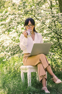 Full length of young woman using phone while sitting on grass