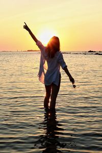 Rear view of silhouette woman standing in sea against orange sky