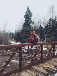 Rear view of girl sitting on bridge in winter
