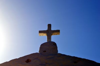 Low angle view of cross on old building against clear blue sky during sunny day