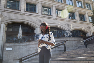 Smiling businesswoman listening music while walking on staircase in city