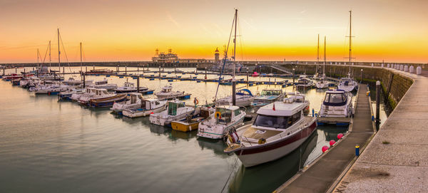 Boats moored in harbor at sunset