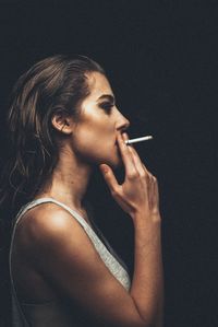 Side view of a young woman smoking over black background