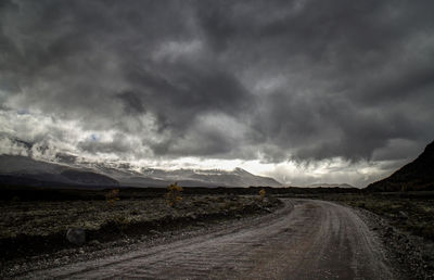 Road passing through landscape against storm clouds