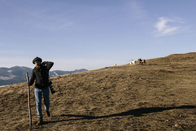 Man hiking with camera and pole on field against sky