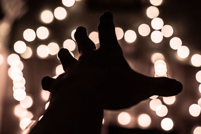 Silhouette hand of person against illuminated lights at night