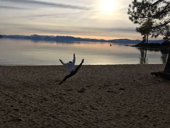 Rear view of mid adult man with arms raised jumping at sandy beach