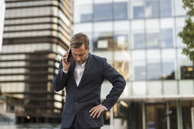 Tensed businessman talking on smart phone in front of office building